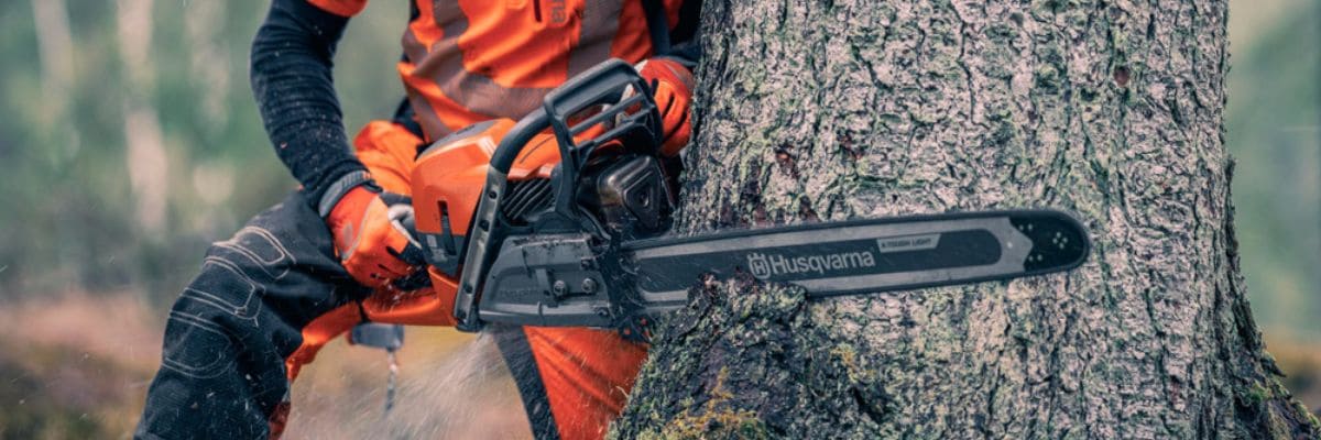 Homme coupant un arbre avec une tronçonneuse Husqvarna